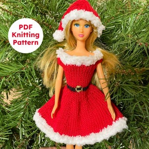 以下が含まれることがあります： 赤いニットのクリスマスドレスと白いトリム、お揃いの帽子をかぶった人形。ドレスには、金のバックルが付いた黒いベルトが付いています。人形は緑の松の針の背景に設定されています。「PDF Knitting Pattern」というテキストが含まれています。