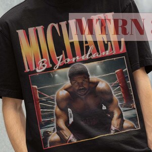 Peut inclure: T-shirt noir avec un imprimé graphique d'un boxeur, Michael B. Jordan, dans un ring de boxe. Le texte "MTRN 38" est visible dans le coin supérieur droit de l'image.
