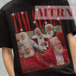May include: Black t-shirt with a graphic print of Tim Allen as Santa Claus from the movie "The Santa Clause". The text "Tim Allen" is printed in red on the shirt.