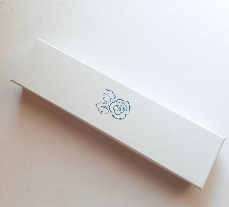 May include: A white rectangular box with a blue rose design printed on the top.