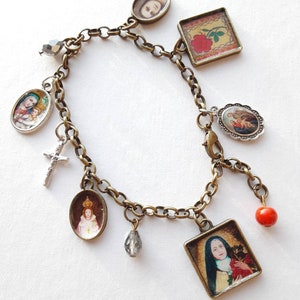 May include: A gold chain bracelet with multiple charms, including a cross, a red bead, a crystal, and several oval and square charms with religious images.