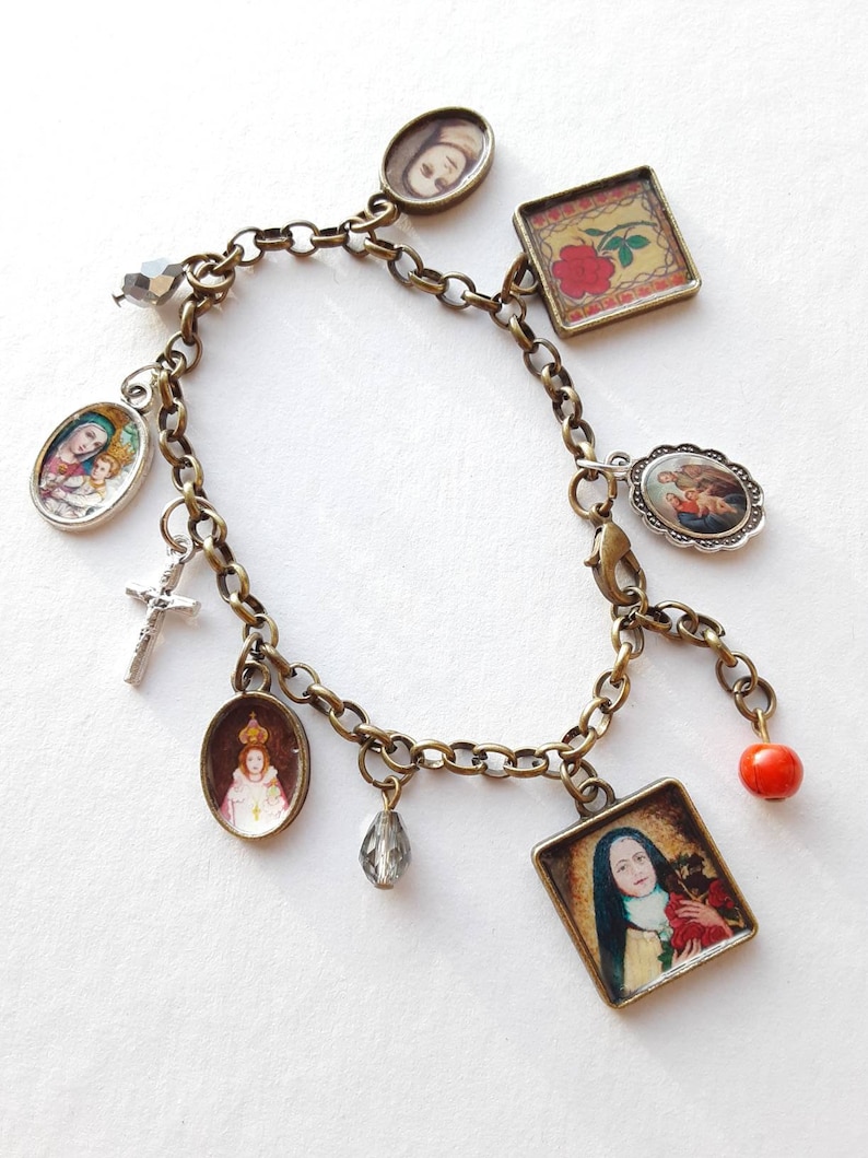 May include: A gold chain bracelet with multiple charms, including a cross, a red bead, a crystal, and several oval and square charms with religious images.