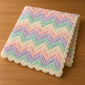 May include: A crocheted baby blanket with a chevron pattern in pastel pink, green, and purple colours. The blanket has a scalloped edge.