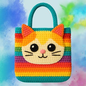 Puede incluir: Una bolsa de mano de crochet de arcoíris con una linda carita de gato en la parte delantera. La bolsa tiene un diseño brillante y colorido con rayas rojas, naranjas, amarillas, verdes, azules y moradas.
