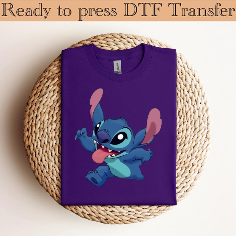 May include: A purple t-shirt featuring a cartoon character, Stitch, with blue and pink accents. The character is smiling with its tongue out. The text "Ready to press DTF Transfer" is at the top.