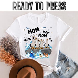 May include: White t-shirt with a graphic of five cartoon seagulls with the word "MOM" repeated around them. The seagulls are on a rock with a blue ocean and fish in the background.