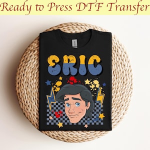 May include: Black t-shirt featuring the name "ERIC" in yellow and blue retro font. The shirt has a graphic of a cartoon character with blue eyes and black hair, surrounded by stars and lightning bolts. The text "Ready to Press DTF Transfer" is at the top.