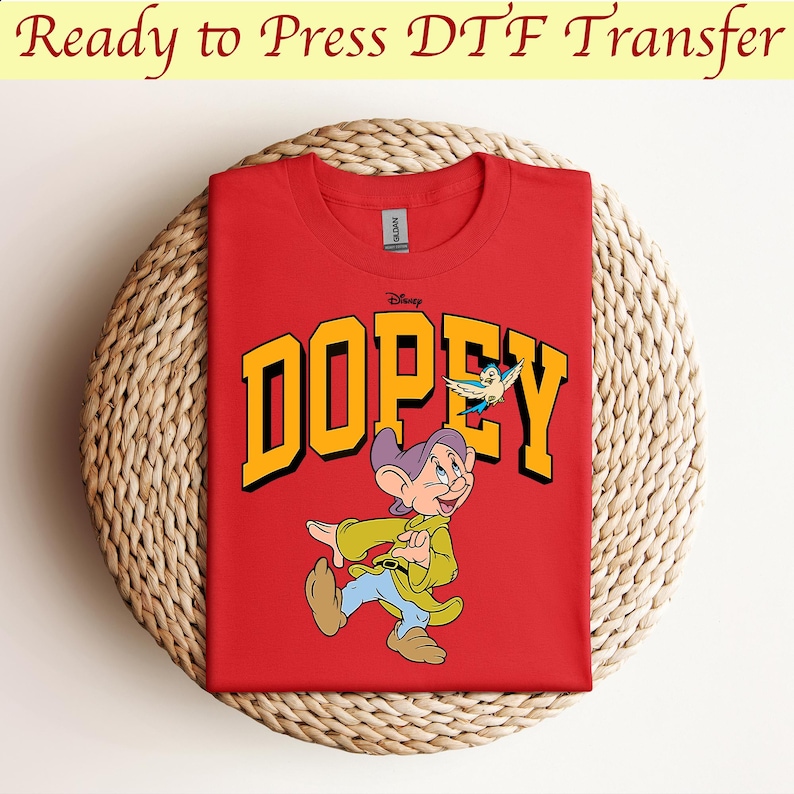 May include: Red t-shirt with a yellow "DOPEY" graphic featuring a cartoon image of Dopey from Disney's Snow White and the Seven Dwarfs. The graphic also includes a small blue bird.