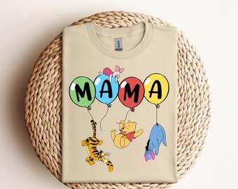 May include: A beige t-shirt featuring a graphic of Winnie the Pooh and his friends holding balloons that spell out "MAMA".