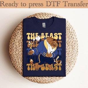 May include: Navy blue t-shirt featuring a colorful illustration of the Beast from Beauty and the Beast. The design includes the text "THE BEAST" in a retro font, along with other characters from the movie. The shirt is ready to press DTF transfer.