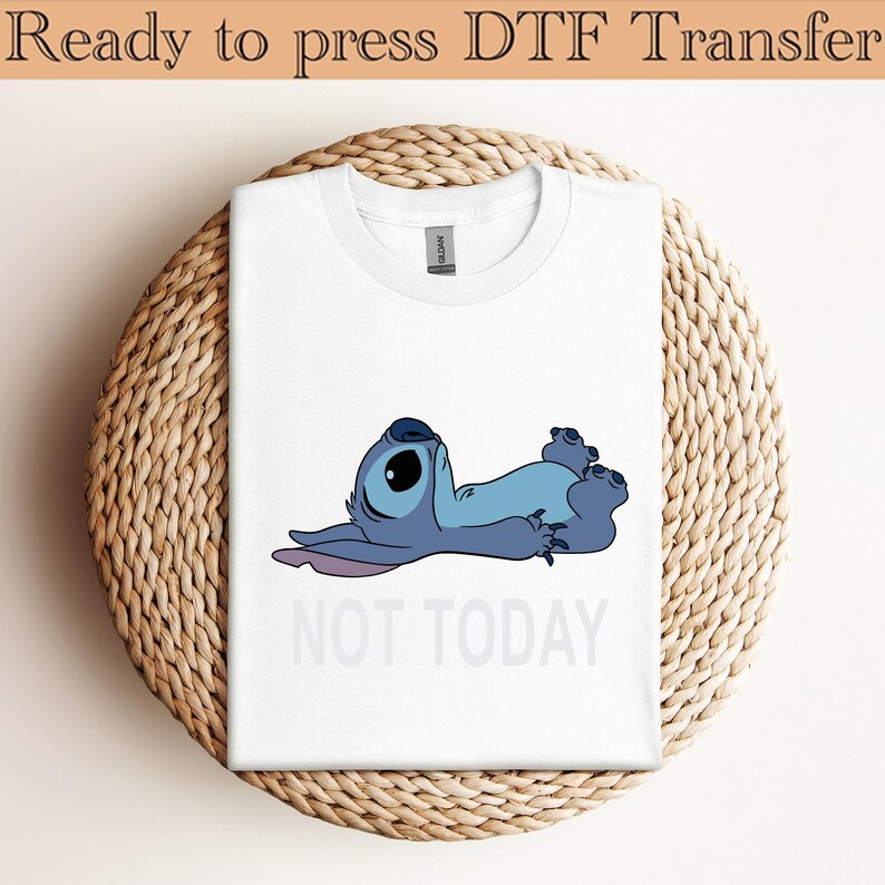 K&ouml;nnte beinhalten: Ein wei&szlig;es T-Shirt mit einer Grafik eines blauen Alien-Charakters, der auf dem R&uuml;cken liegt und die Augen geschlossen hat. Unter der Figur steht der Text NOT TODAY in hellgrauen Gro&szlig;buchstaben. Das T-Shirt hat einen Rundhalsausschnitt.