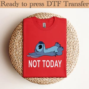 K&ouml;nnte beinhalten: Ein leuchtend rotes T-Shirt mit einer Grafik eines blauen Alien-Charakters, der auf dem R&uuml;cken liegt, darunter der Text NOT TODAY in wei&szlig;en Gro&szlig;buchstaben. Das T-Shirt hat einen Rundhalsausschnitt und eine klassische Kurzarm-Konstruktion.