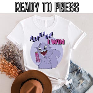 Puede incluir: Camiseta blanca con un gato de dibujos animados morado que sostiene una botella rosa y dice "AHA HA HA! I WIN".