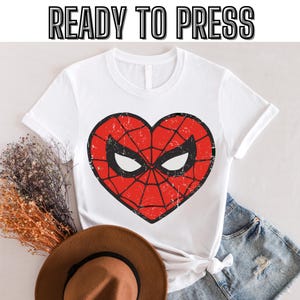 May include: White t-shirt with a red heart-shaped graphic of Spider-Man's mask. The graphic has a distressed look and the text "READY TO PRESS" is at the top of the image.
