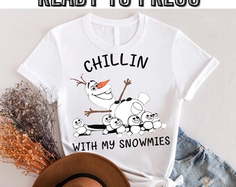 Puede incluir: Camiseta blanca con un gráfico en blanco y negro de Olaf de Frozen. El gráfico muestra a Olaf sentado en una pila de muñecos de nieve con el texto "Chillin' with my snowmies".
