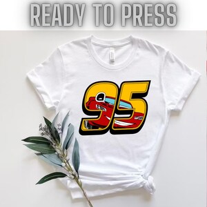 May include: White t-shirt with a yellow and black number 95 design. The number 95 has a red cartoon car inside of it.