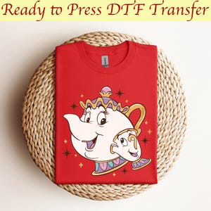 May include: Red t-shirt with a white and gold print of the character Mrs. Potts from Disney's Beauty and the Beast. The print features Mrs. Potts holding a teacup with a smiling face.