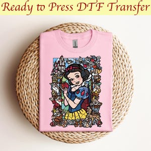 以下が含まれることがあります： ピンクのTシャツに、ステンドグラス風の白雪姫がリンゴを持っている画像がプリントされています。画像には小人や背景に城も含まれています。