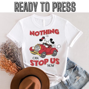 May include: White t-shirt with a red car and Mickey Mouse and Minnie Mouse characters. The text on the shirt reads "Nothing can stop us now".
