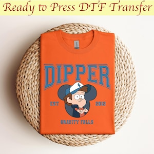 May include: Orange t-shirt with a blue graphic of Dipper Pines from Gravity Falls. The graphic includes the text "Dipper" in a blue collegiate font, "Est. 2012", and a cartoon image of Dipper with a Mickey Mouse ear silhouette.