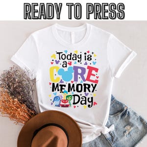 以下が含まれることがあります： 「Today is a CORE MEMORY Day」というカラフルなグラフィックがプリントされた白いTシャツ。COREの文字の中にミッキーマウスの頭が描かれており、映画「インサイド・ヘッド」のキャラクターも描かれている。