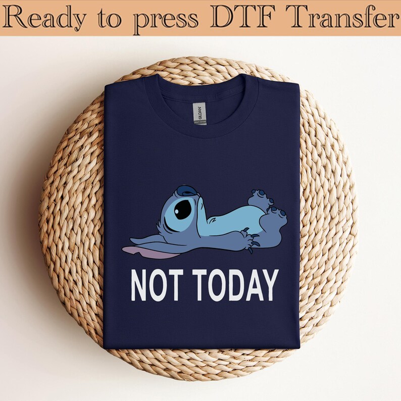 K&ouml;nnte beinhalten: Ein marineblaues T-Shirt mit einer Grafik einer hellblauen Zeichentrickfigur, die auf dem R&uuml;cken liegt, darunter der Text NOT TODAY in wei&szlig;en Gro&szlig;buchstaben. Das T-Shirt hat einen Rundhalsausschnitt und ein klassisches Kurzarm-Design.