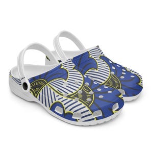 May include: White clogs with a blue, white, and yellow patterned design. The pattern features floral and geometric shapes. The clogs have white straps and a white sole. The clogs are a slip-on style.