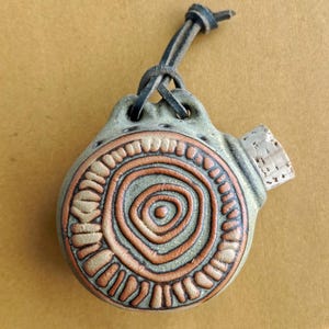May include: Handmade ceramic flask with a spiral design in shades of brown and green. The flask has a leather cord for carrying and a cork stopper. The flask is a unique piece of art.
