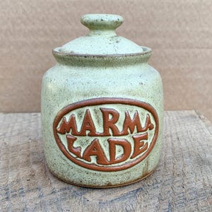 Puede incluir: Un tarro de cerámica verde con tapa, que presenta una etiqueta ovalada marrón que dice "MARMALADE".