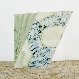 Może przedstawiać: Ceramiczna rzeźba o geometrycznym wzorze. Rzeźba składa się z wielu kawałków gliny ułożonych jeden na drugim. Glina jest jasnozielona z niebieskimi i białymi akcentami.