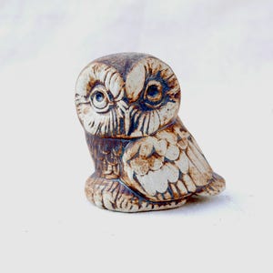 Puede incluir: Una figurita de búho de cerámica con esmalte marrón y blanco. El búho tiene ojos grandes y redondos y plumas detalladas.