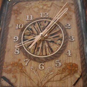 May include: A wooden framed clock with a natural wood background and gold numbers. The clock face is made of wood chips and has gold glitter. The clock hands are gold.