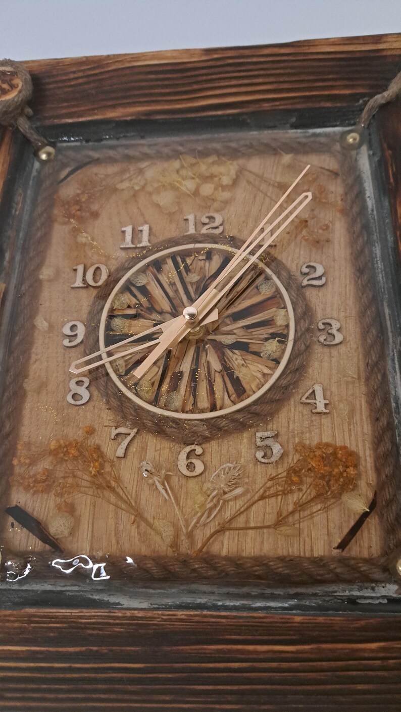 May include: A wooden framed clock with a natural wood background and gold numbers. The clock face is made of wood chips and has gold glitter. The clock hands are gold.