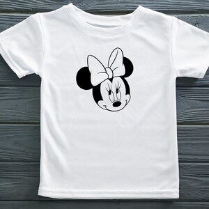 Peut inclure: T-shirt blanc avec une image en noir et blanc de Minnie Mouse avec un n&oelig;ud rouge.