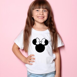 Peut inclure: Un t-shirt blanc avec une image noire et blanche de la t&ecirc;te de Minnie Mouse avec un n&oelig;ud sur le dessus.
