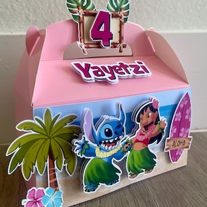 May include: Pink party favor box decorated with a tropical theme. Features the number 4, the name "Yayetzl", and cartoon characters Stitch and Lilo. Includes a palm tree, flowers, and a surfboard with the word "Aloha".