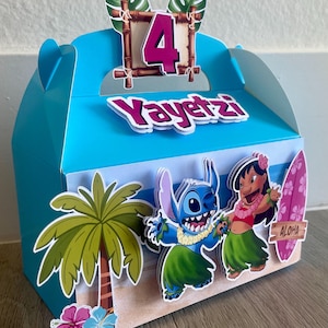 May include: A blue party favor box with a tropical theme. The box features a palm tree, cartoon characters, and the number 4. The name "Yayetz" is displayed on the front. The box has a handle and is decorated with a surfboard that says "Aloha".