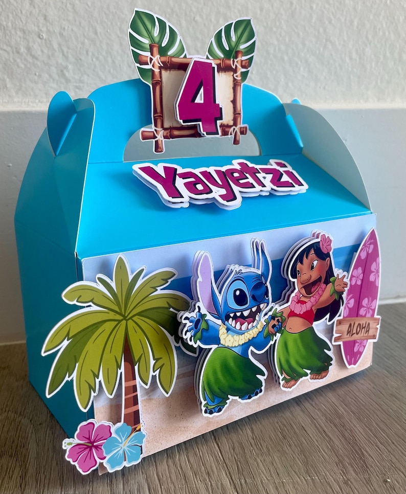 May include: A blue party favor box with a tropical theme. The box features a palm tree, cartoon characters, and the number 4. The name "Yayetz" is displayed on the front. The box has a handle and is decorated with a surfboard that says "Aloha".