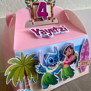 May include: Pink party favor box decorated with a tropical theme. Features the number 4, the name "Yayetz", and cartoon characters Stitch and Lilo. Includes a palm tree, flowers, and a surfboard with "Aloha" text.