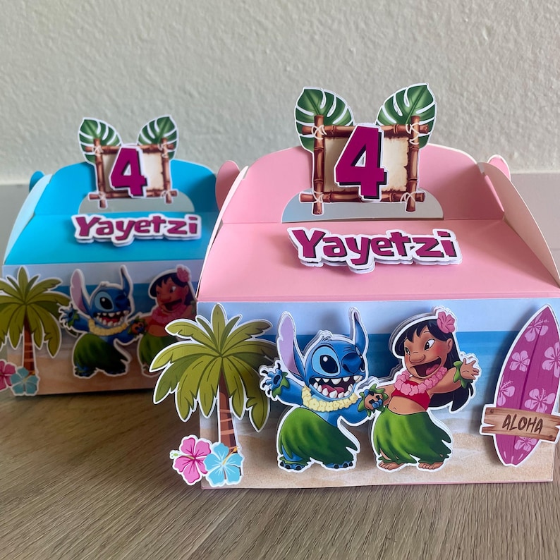May include: Two colorful party favor boxes, one blue and one pink, feature a tropical beach scene with cartoon characters. Each box has the number "4" and the name "Yayetz" on top. The boxes are decorated with palm trees and a surfboard.