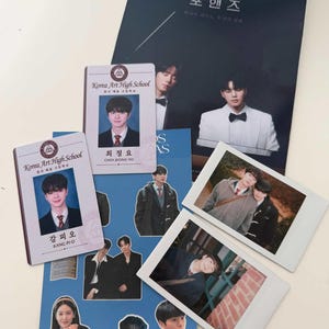 Può includere: Una collezione di materiale stampato che include due tessere studentesche della Korea Art High School per Choi Jeong-yo e Kang Pi-o, un poster blu scuro con testo coreano, un foglio di adesivi con vari ritratti e due stampe fotografiche.
