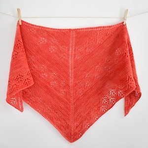 Può includere: Uno scialle di maglia color corallo con un delicato motivo a pizzo è appeso a uno stendino.