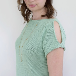 May include: A light green knitted top with a scoop neck and short sleeves. The sleeves have cutouts at the shoulders. The top is worn with a gold necklace.