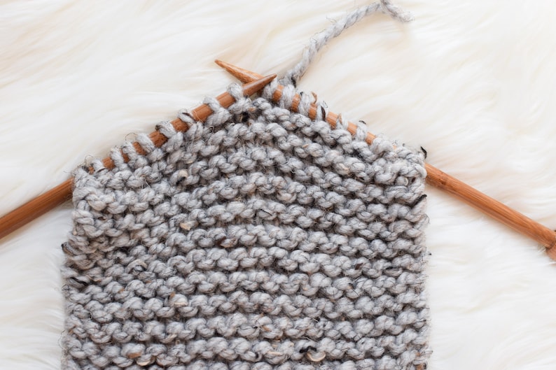 A work in progress photo of a grey marble (lighter grey) scarf on bamboo knitting needles.