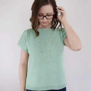 May include: A light green knitted top with short sleeves and a scoop neck. The top is made of a soft, lightweight fabric and has a relaxed fit.