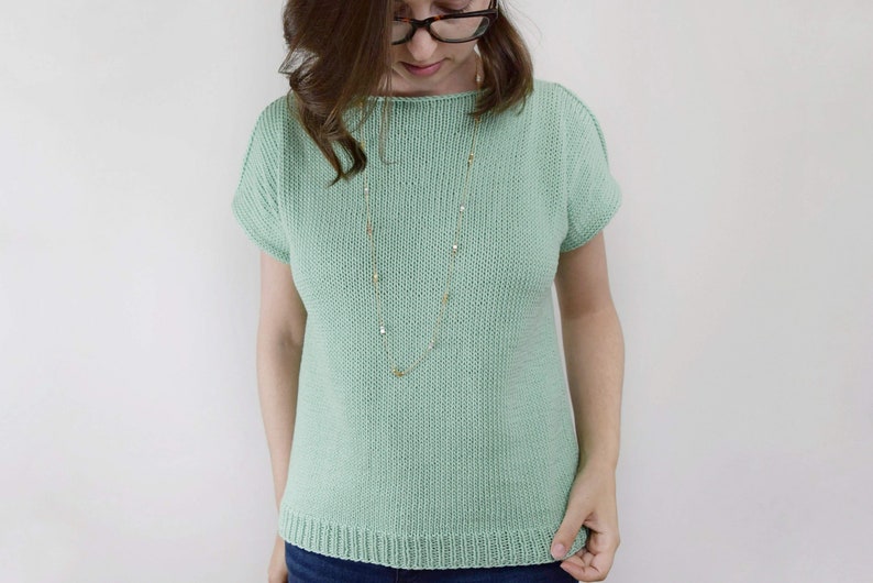 May include: A light green knitted top with short sleeves. The top has a round neckline and a relaxed fit.