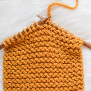 A work in progress photo of a mustard scarf on bamboo knitting needles.