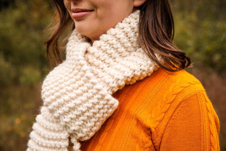 A close up shot of a woman wearing the finished cream colored scarf.