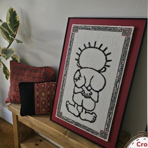 以下が含まれることがあります： デジタルダウンロード可能なPDF形式のクロスステッチパターン。黒と白のイラストで、とげとげの髪をした子供が描かれています。パターンは額装され、赤い背景の棚に飾られています。画像の上部には「デジタルダウンロードPDF」というテキストがあります。画像の下部には「クロスステッチパターンのみ」というテキストがあります。画像の下部には「すべての収益は、このデザインを作成したガザに拠点を置くアーティストを支援するために使われます」というテキストがあります。