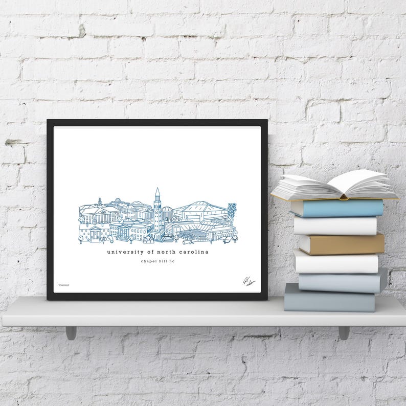 May include: A black framed print of a blue line drawing of the University of North Carolina campus, including the bell tower and the Dean Smith Center. The text "University of North Carolina" and "Chapel Hill, NC" is below the drawing.